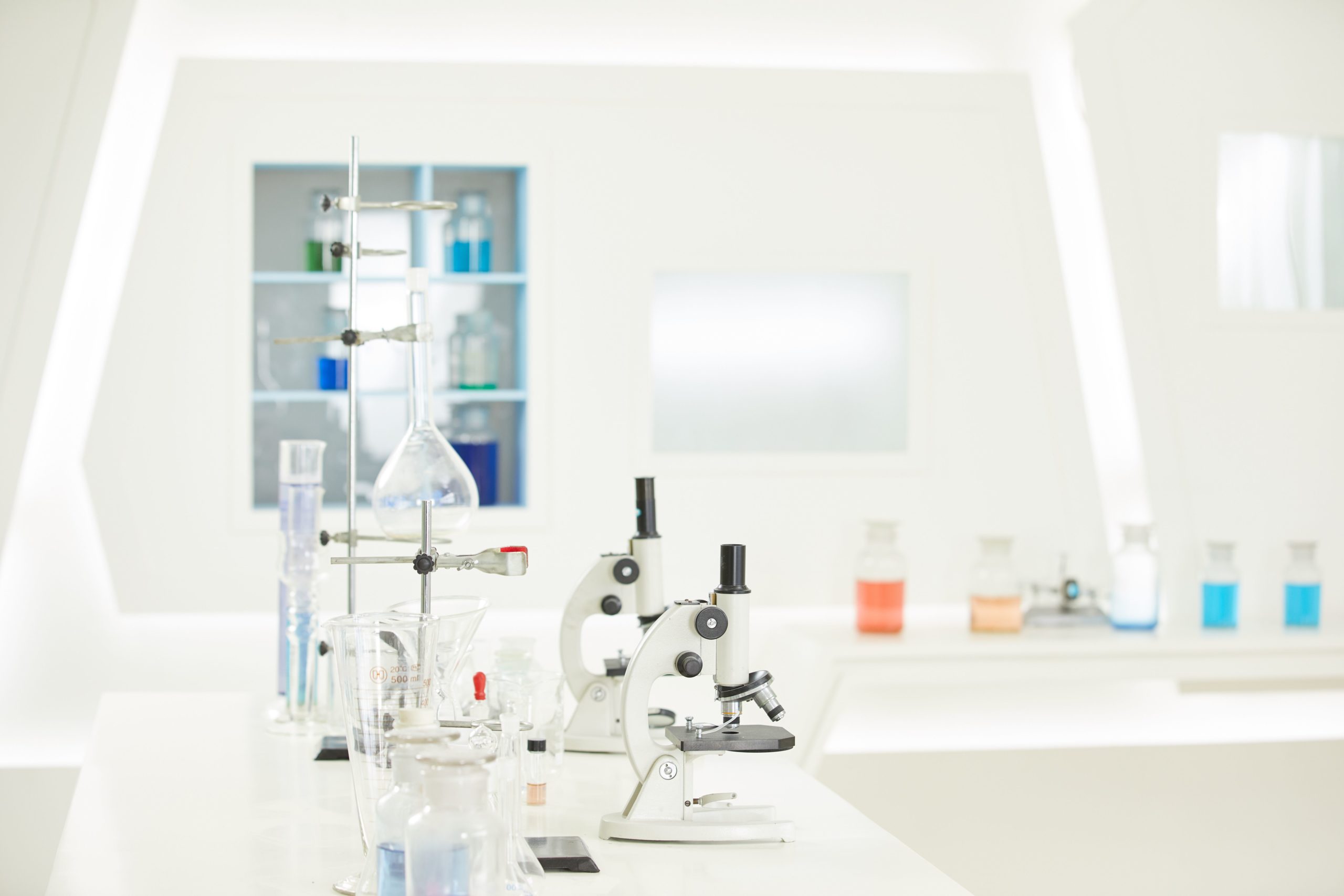 Side view of two microscopes next to beakers filled with fluid and other laboratory equipments.